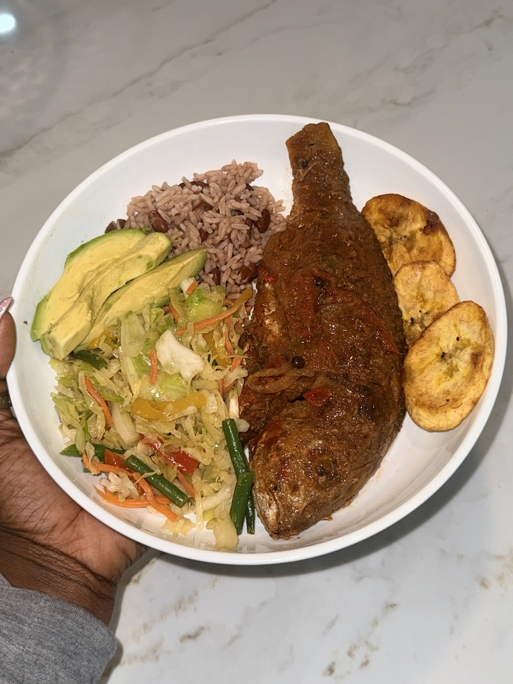 A colorful Caribbean plate with snapper, rice and peas, cabbage, plantain, and avocado