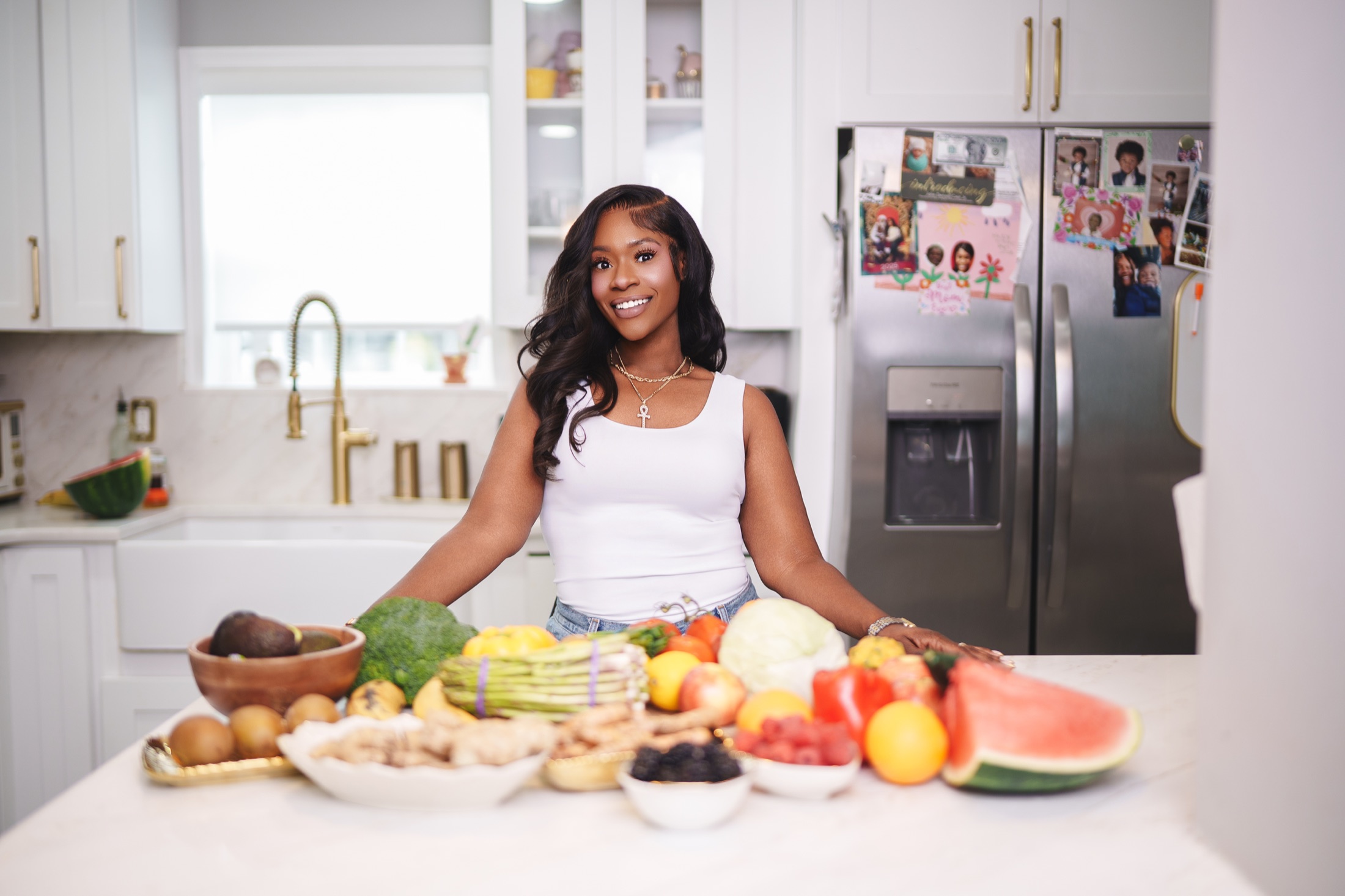 Meisha smiling behind a colorful spread of fresh produce in her kitchen