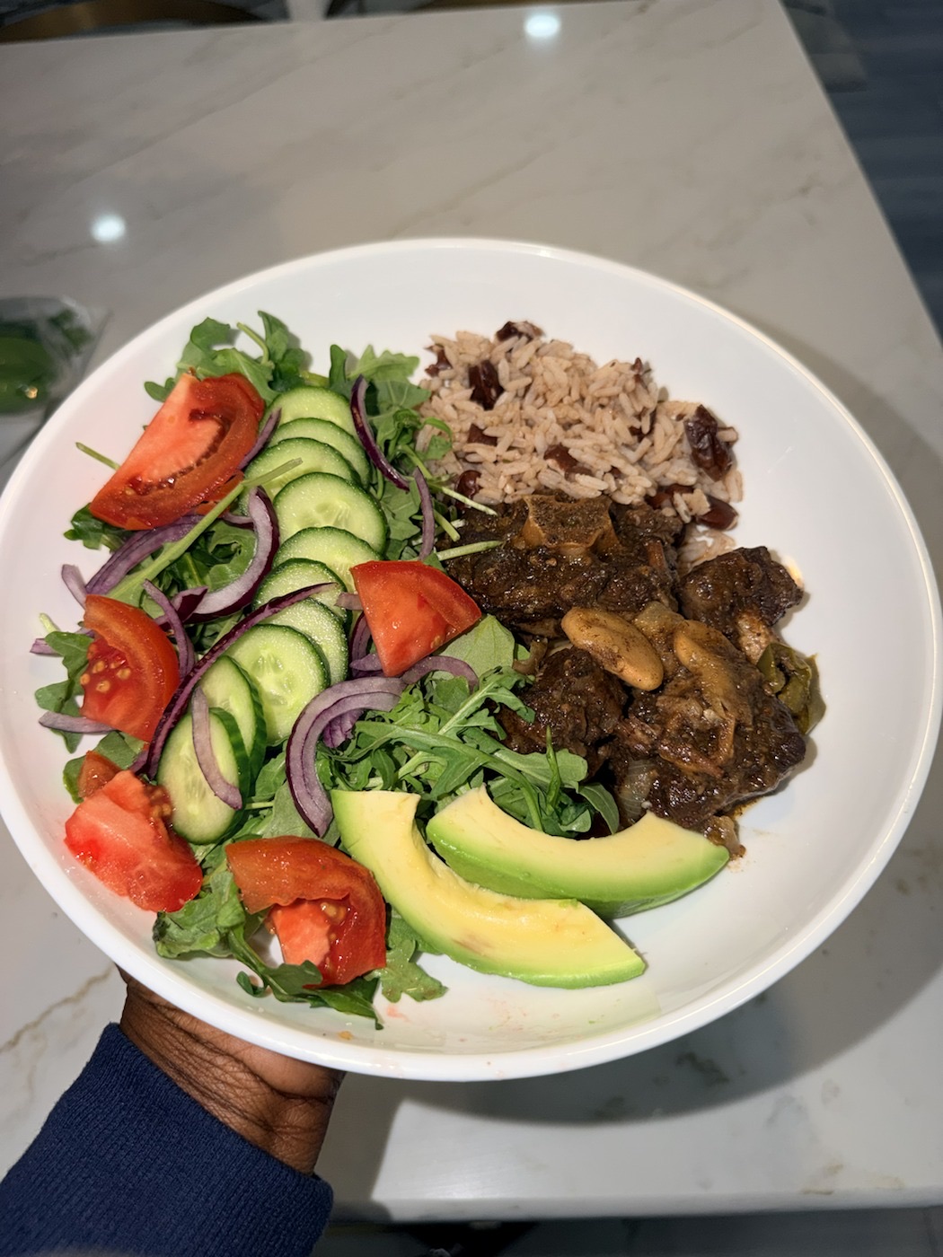 A plate with oxtail, rice and peas, and a colorful salad